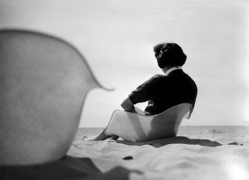 Una foto degli anni 60 ritrae su una spiaggia una donna che legge seduta sul guscio di una sedia DSW